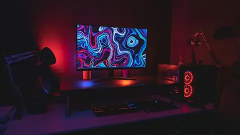 Postazione da gioco in penombra con luci rosse e monitor acceso